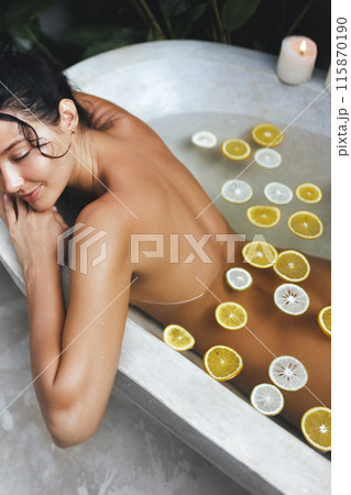 Serene Woman Relaxing in Citrus Bath with Candles in Tropical Setting 115870190