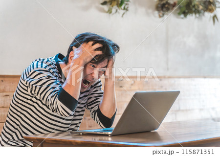 カフェ・飲食店でパソコンを見ながら頭を抱えるアジア人男性（株・投資・暴落・損害） 115871351