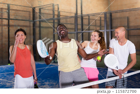 Four smiling men and women with padel rackets posing at court 115872700