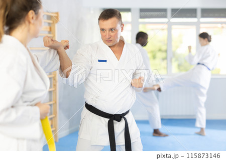 Woman and man in kimono sparring in gym during karate training Woman and man in kimono sparring in gym during karate training 115873146