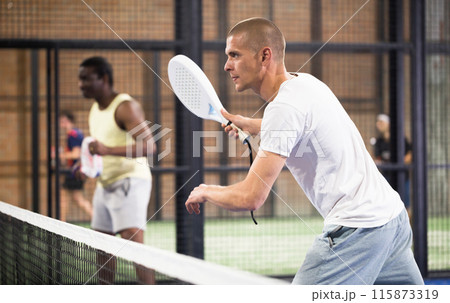 Focused man playing paddle ball match on closed court Focused man playing paddle ball match on closed court 115873319