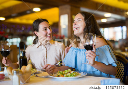 Two girls are discussing something fun at a table in restaurant 115873332