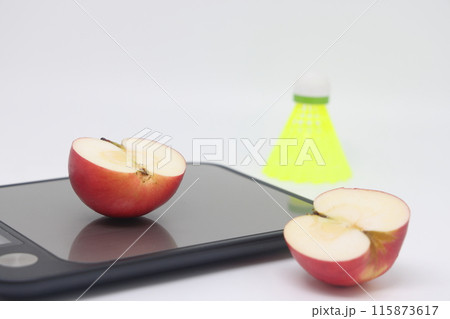 An apple on a kitchen scale against a backgroud of a shuttlecock. Calorie counting An apple on a kitchen scale against a backgroud of a shuttlecock. Calorie counting 115873617