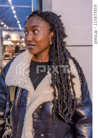 A trendy woman wrapped in a cozy coat gazes contemplatively at the city lights on a winter evening 115873859