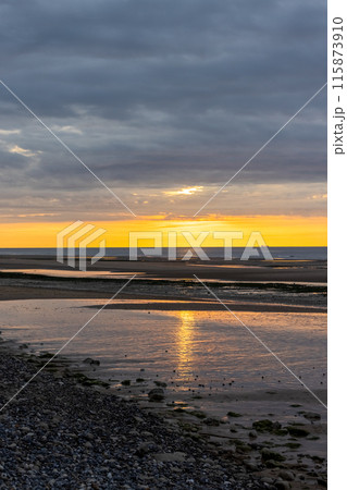 Witness the beauty of a stunning sunset over the beach, with reflective water and a dramatic sky 115873910