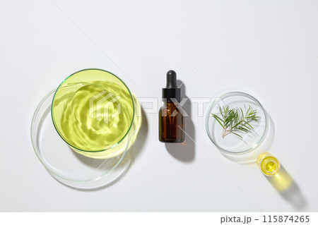 Natural and organic cosmetic concept with a glass serum bottle displayed with three petri dishes and a beaker of tea tree oil. Skincare concept with empty label 115874265