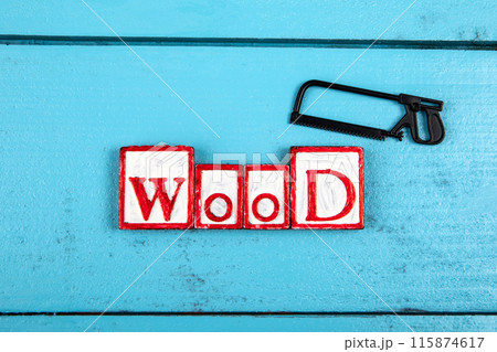 WOOD. Miniature saw on a blue wooden background. Construction and carpentry concept 115874617