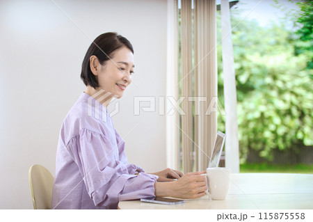 リビングでコーヒーを飲みながらパソコンを見るミドル女性 115875558