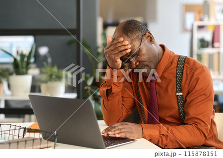Portrait of senior man struggling at work with head in hands and using laptop copy space 115878151