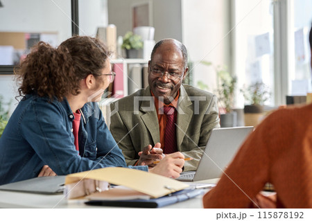 Portrait of smiling senior man talking to young colleague in business meeting and enjoying work in age inclusive office copy space 115878192