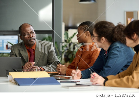Portrait of senior African American man leading business meeting in office and listening to group of young employees copy space Portrait of senior African American man leading business meeting in office and listening to group of young employees copy space 115878210