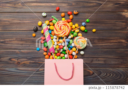 shopping paper gift bag in corner full of assorted traditional candies falling out on colored background with copy space. Happy Holidays sale concept shopping paper gift bag in corner full of assorted traditional candies falling out on colored background with copy space. Happy Holidays sale concept 115878742