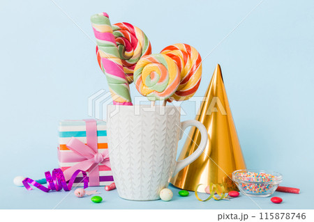 Colorful candies in cup on table on light background background. Large swirled lollipops. Creative concept of a jar full of delicious sweets from the candy store Colorful candies in cup on table on light background background. Large swirled lollipops. Creative concept of a jar full of delicious sweets from the candy store 115878746