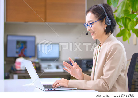 オフィスで仕事をするヘッドセットを付けたミドル女性 115878869