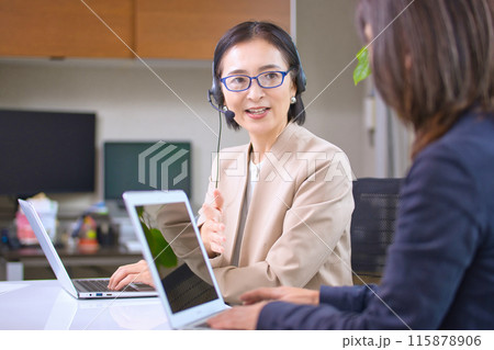 オフィスで仕事をするヘッドセットを付けたミドル女性 115878906