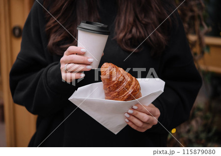 Woman holding coffee and croissant outdoors 115879080