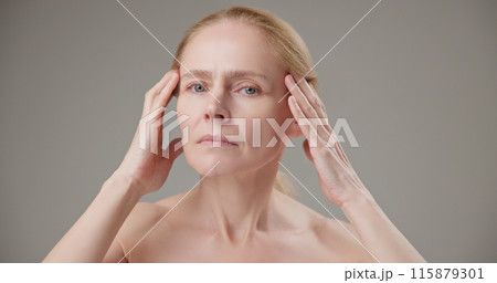 Anti age, Beauty, health and dry skin care concept - beautiful middle-aged mature Caucasian woman in her 50s touching her face skin and looking at the camera with a slight smile 115879301