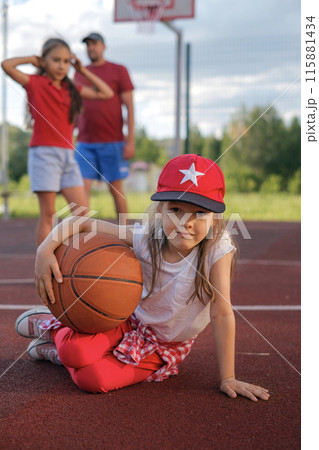 A cute little girl in a baseball cap sits with a basketball on the playground after a game A cute little girl in a baseball cap sits with a basketball on the playground after a game 115881434