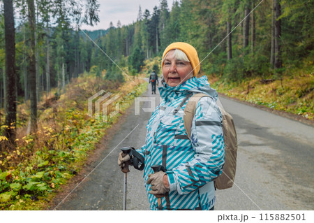 Mature caucasian blonde woman on vacation, having a hike in autumn mountains with backpack and hiking poles, enjoying adventure. 115882501