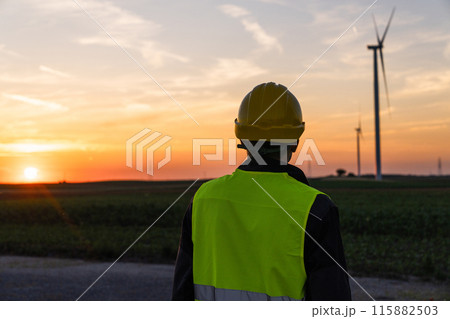 Worker looks at wind turbines at sunset. 115882503