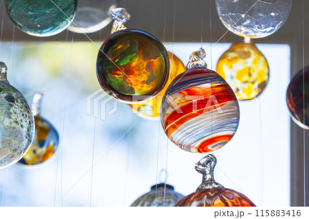 Colorful transparent glass balls hang in front of bright window, close up Colorful transparent glass balls hang in front of bright window, close up 115883416