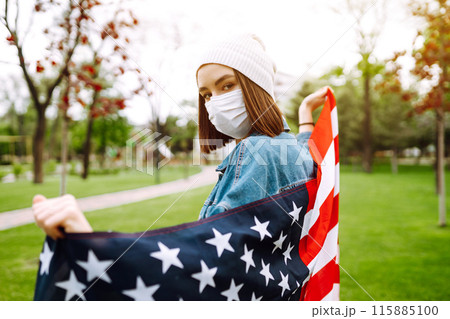Girl in protective sterile medical mask and with american flag in hand. Quarantine city. Covid -19. Girl in protective sterile medical mask and with american flag in hand. Quarantine city. Covid -19. 115885100