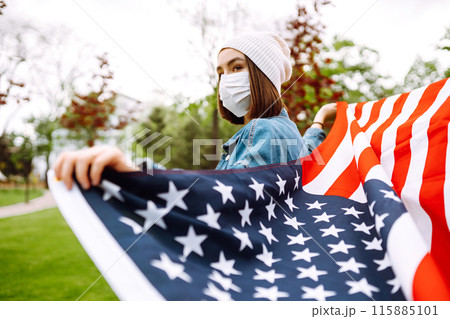Girl in protective sterile medical mask and with american flag in hand. Quarantine city. Covid -19. Girl in protective sterile medical mask and with american flag in hand. Quarantine city. Covid -19. 115885101