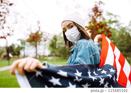 Girl in protective sterile medical mask and with american flag in hand. Quarantine city. Covid -19. 115885102