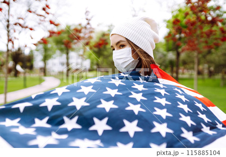 Girl in protective sterile medical mask and with american flag in hand. Quarantine city. Covid -19. Girl in protective sterile medical mask and with american flag in hand. Quarantine city. Covid -19. 115885104