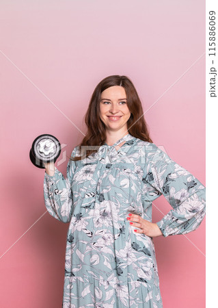Happy Pregnant Woman Lifting Dumbbell in Floral Dress 115886069