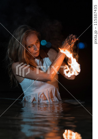 Caucasian woman dancing with fire in the water. Fire show at sea. Acrobatics on the beach. Yoga and relaxation at sunset. Spectacular circus performance. model body. High quality FullHD footage.  115887435
