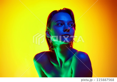 Portrait of young woman with bare shoulders posing looking away in neon light against gradient studio background. Well-cared-for skin. 115887568