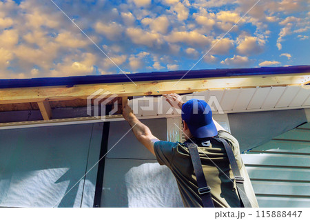 Placing vinyl soffit plastic boards on roof rafters in new building Placing vinyl soffit plastic boards on roof rafters in new building 115888447