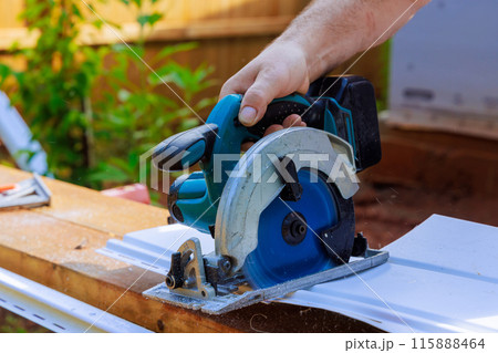 As part of construction of facade of craftsman, he cuts the vinyl siding panel to desired size before it is installed 115888464