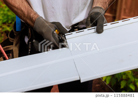 In course of construction, craftsman cuts vinyl siding panels to desired size before installing them In course of construction, craftsman cuts vinyl siding panels to desired size before installing them 115888481