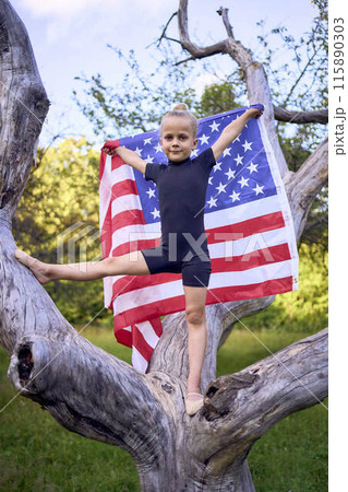 a little 5-year-old gymnast in a black minimalist jumpsuit is practicing with the flag of USA in the garden a little 5-year-old gymnast in a black minimalist jumpsuit is practicing with the flag of USA in the garden 115890303