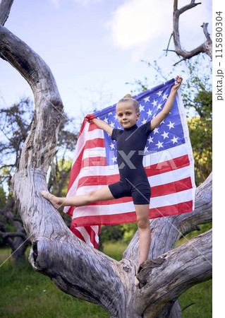 a little 5-year-old gymnast in a black minimalist jumpsuit is practicing with the flag of USA in the garden a little 5-year-old gymnast in a black minimalist jumpsuit is practicing with the flag of USA in the garden 115890304