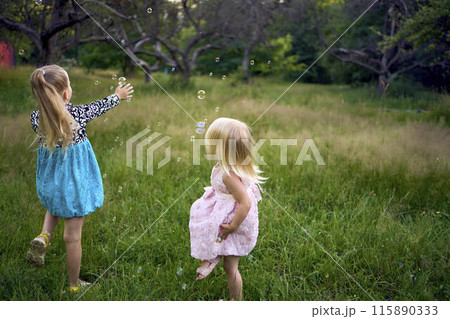 child and toddler, sisters, catching bubbles in the garden child and toddler, sisters, catching bubbles in the garden 115890333