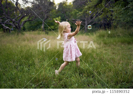 a toddler in a pink cloud dress catches soap bubbles in the garden 115890352