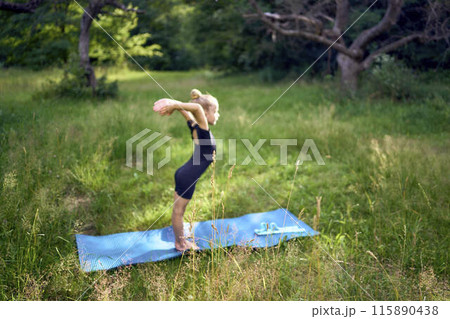 little 5-year-old girl in a black minimalist overall does gymnastics in the garden, outdoors little 5-year-old girl in a black minimalist overall does gymnastics in the garden, outdoors 115890438