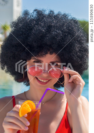 Cheerful charming sexy woman drinking a drink near the pool at the resort, long-awaited vacation concept 115890630
