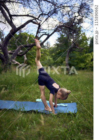 little 5-year-old girl in a black minimalist overall does gymnastics in the garden, outdoors 115890662