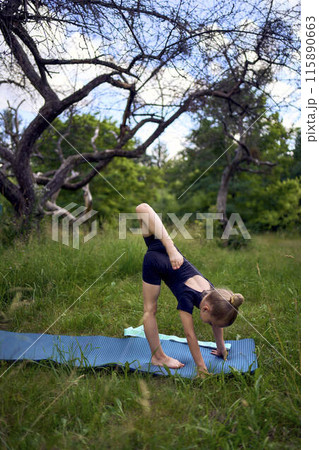 little 5-year-old girl in a black minimalist overall does gymnastics in the garden, outdoors 115890663