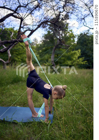 little 5-year-old girl in a black minimalist overall does gymnastics in the garden, outdoors 115890670