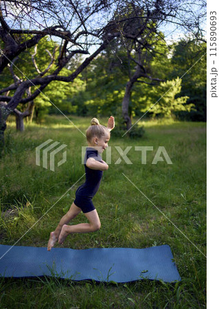 little 5-year-old girl in a black minimalist overall does gymnastics in the garden, outdoors little 5-year-old girl in a black minimalist overall does gymnastics in the garden, outdoors 115890693
