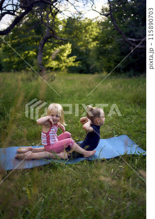 a little 5-year-old gymnast in a black minimalist jumpsuit shows her toddler sister exercises 115890703