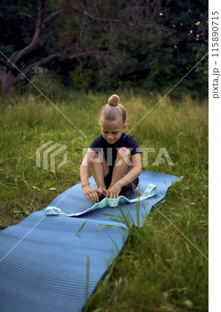 a little 5-year-old girl in a black minimalist jumpsuit does gymnastics in the garden, outdoors 115890715