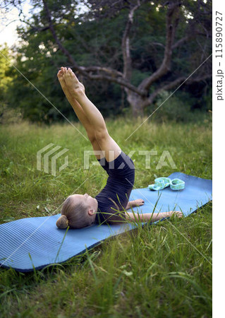 a little 5-year-old girl in a black minimalist jumpsuit does gymnastics in the garden, outdoors 115890727
