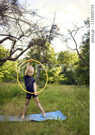 little 5-year-old gymnast in a black minimalistic leotard exercises with a hoop in the garden 115890735