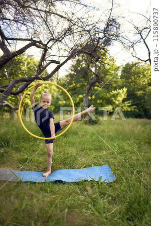 little 5-year-old gymnast in a black minimalistic leotard exercises with a hoop in the garden 115890737